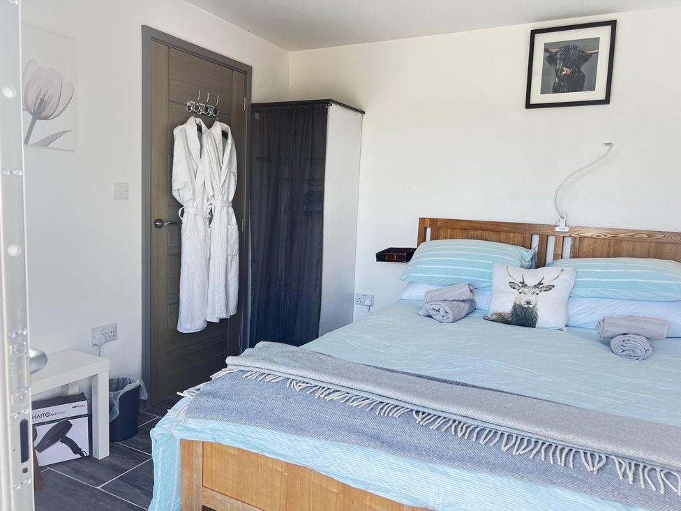 A bedroom with a bed and bathrobes hanging in a wardrobe at The lodge at Plumstone View Haverfordwest