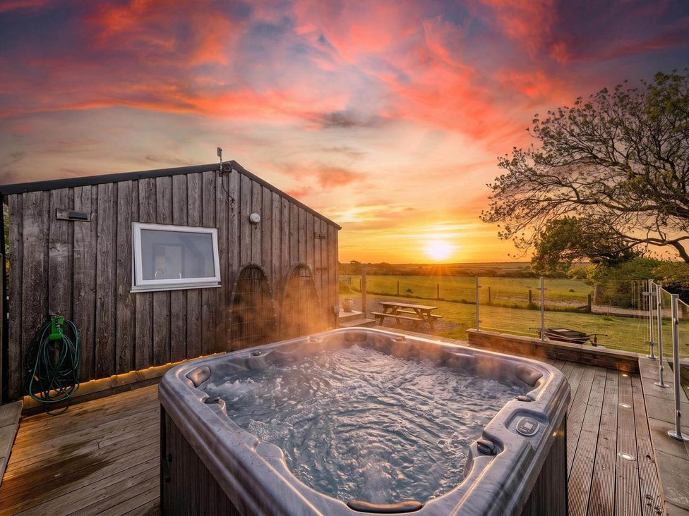 A hot tub next to a wooden building during sunset at The lodge at Plumstone View in Letterston