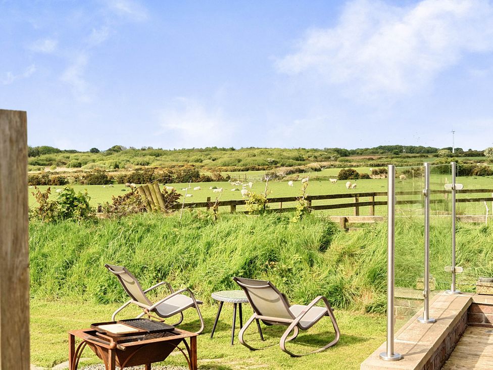 A garden with chairs and a table overlooking sheep in a field at The lodge at Plumstone View in Letterston