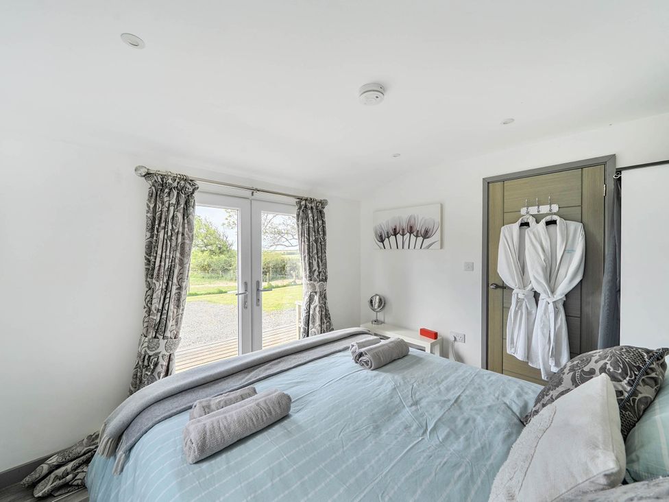 A bedroom with a bed and double doors opening to the outside at The lodge at Plumstone View Letterston