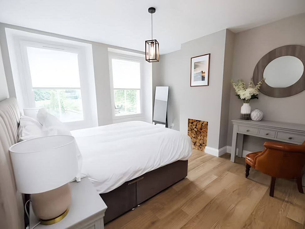 A bedroom with a bed, table, and windows at Robert the Bruce Apartment in Dunfermline