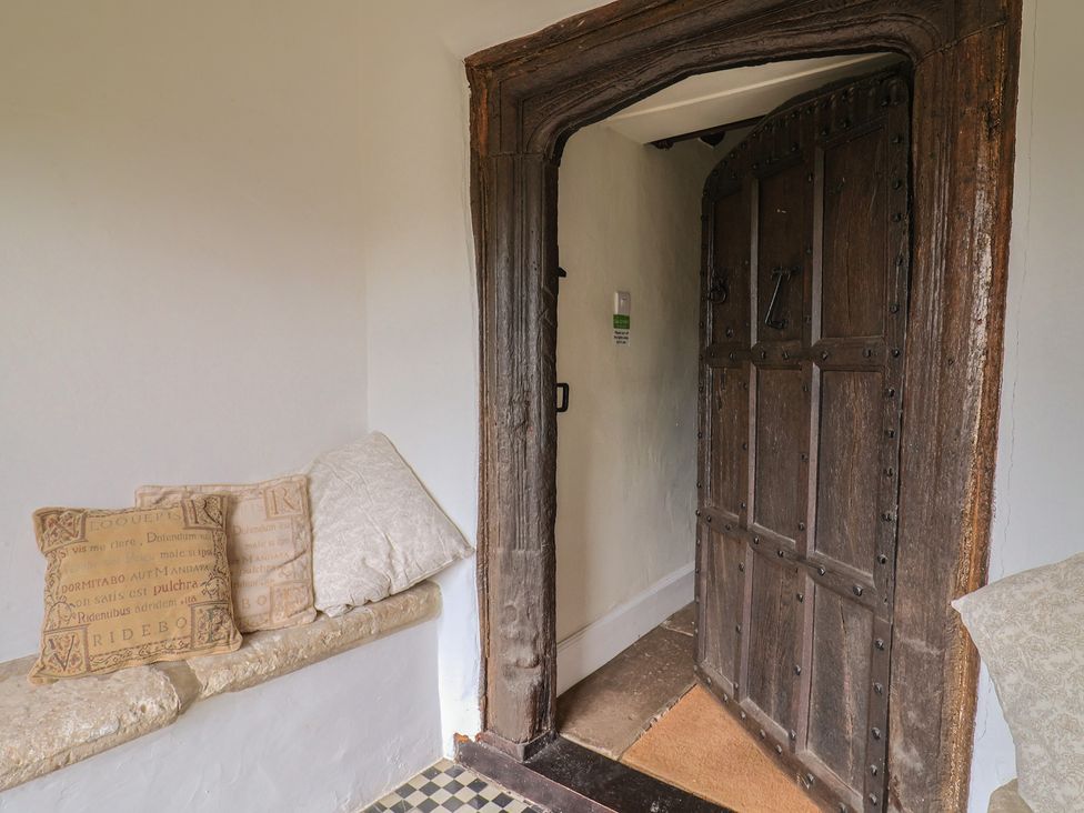 An entrance with a large wooden door and cushions on a stone bench at Ellishayes Farm in Combe Raleigh