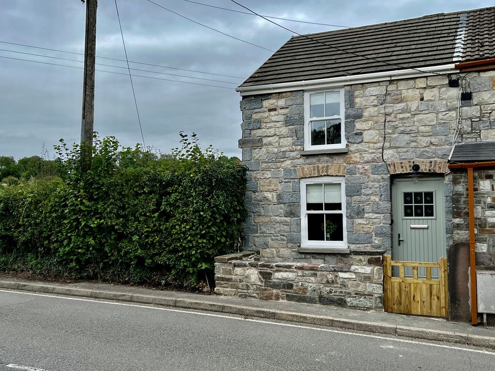 A stone house with a hedge and street at Penderyn Cottage Aberdare