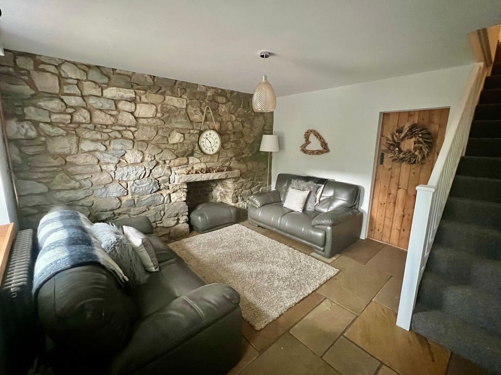 A living room with a stone wall and sofas at Penderyn Cottage in Aberdare