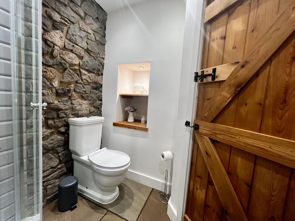 A bathroom with a toilet and stone wall at Penderyn Cottage in Aberdare
