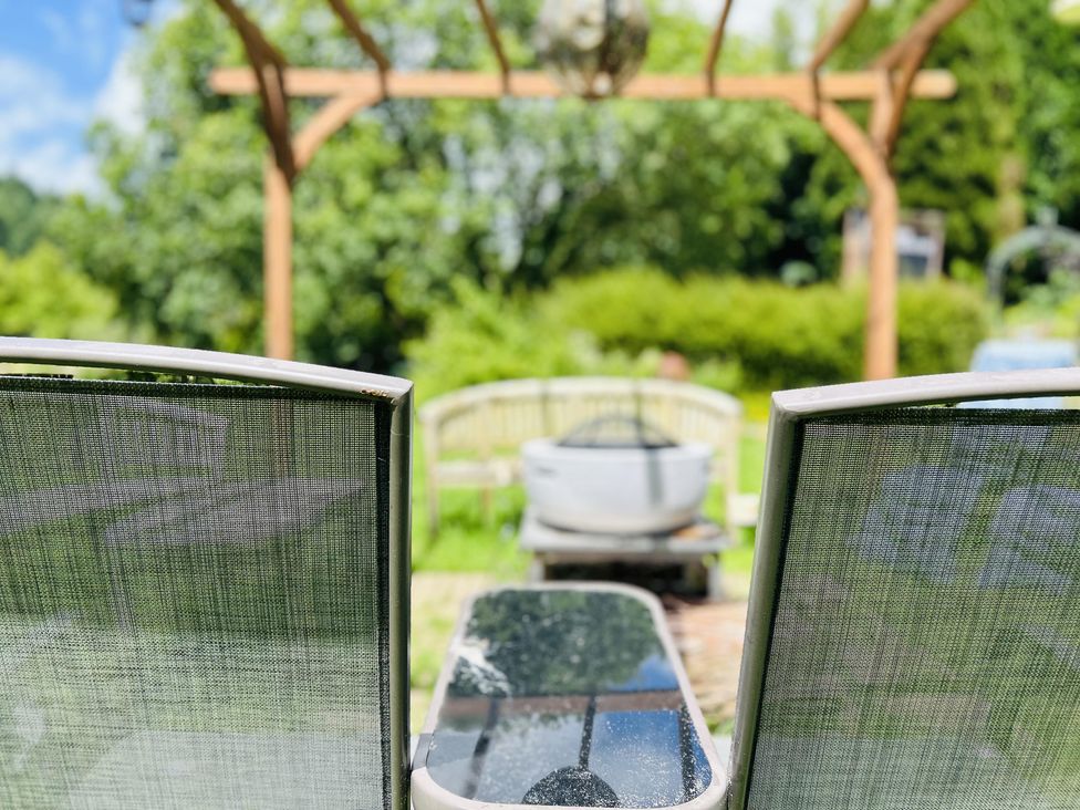 A garden with chairs and a table under a wooden pergola at The Bark House in Tiverton