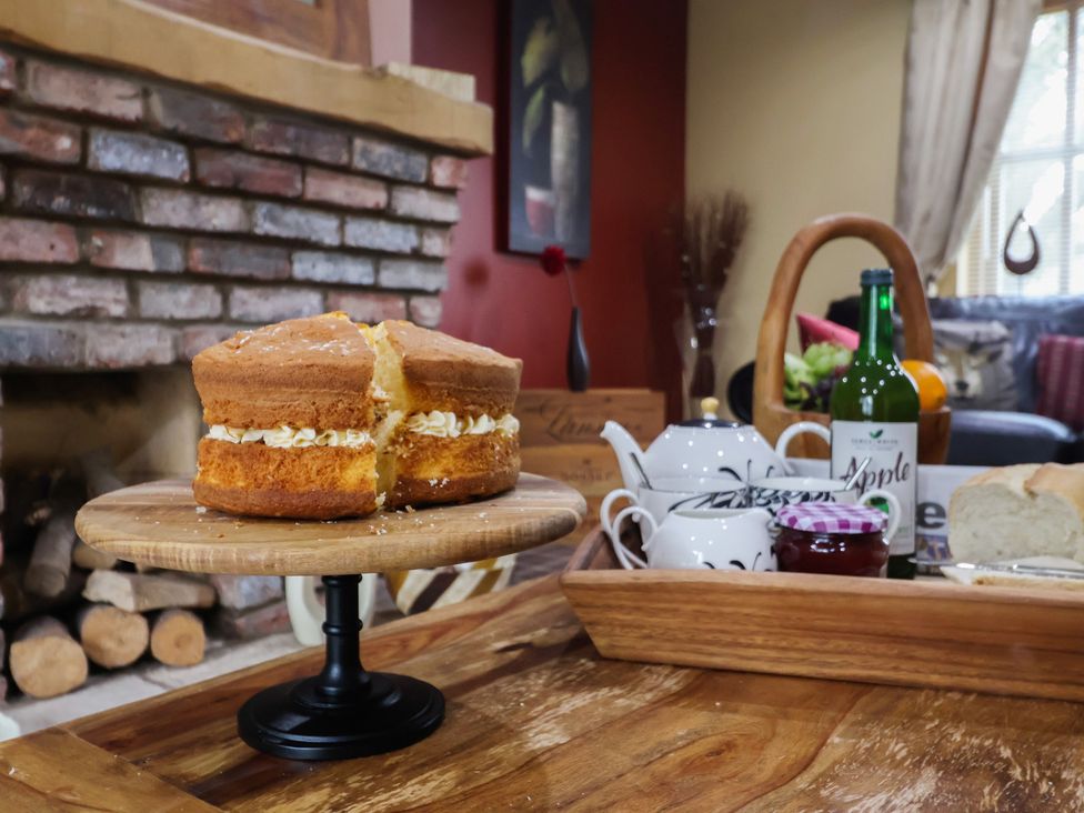 A cake on a wooden cake stand with tea set in a living room at Champagne Cottage in Malton