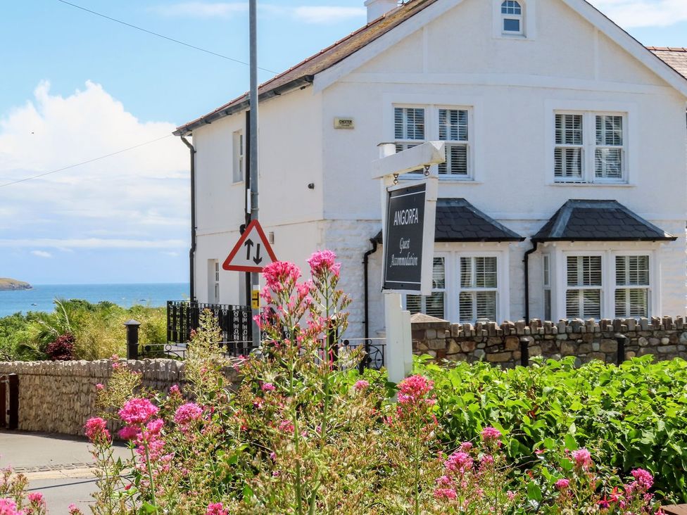 A house with a sign in front and flowers at Angorfa Apartment in Abersoch