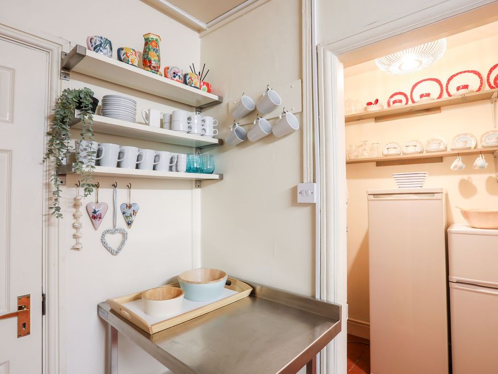 A kitchen with shelves holding mugs and dishes at Angorfa Apartment in Abersoch