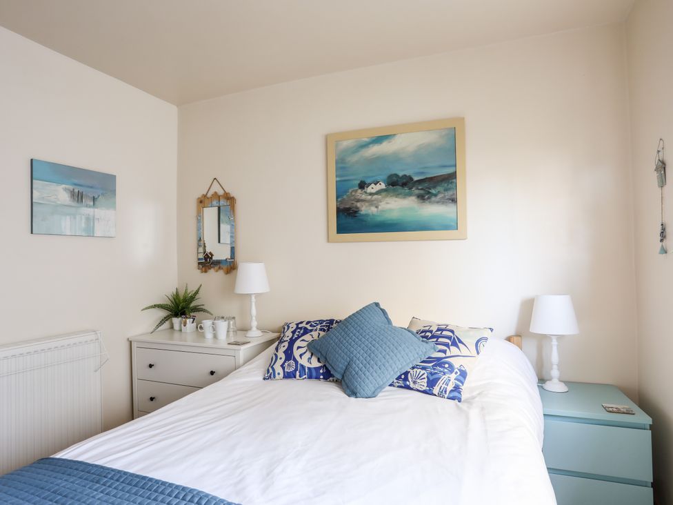 A bedroom with a bed, nightstand, and paintings at Angorfa Apartment in Abersoch
