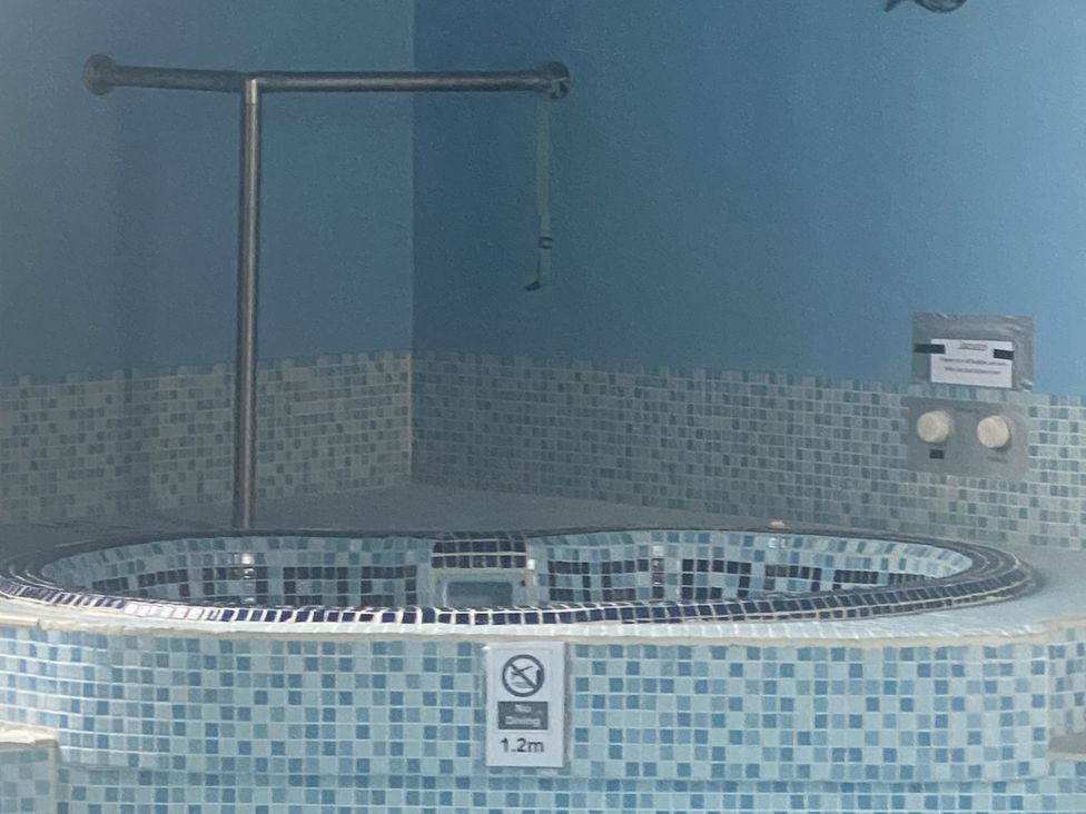 A bathtub with mosaic tiles and a handrail at Honeypot Cottage Whitchurch Canonicorum