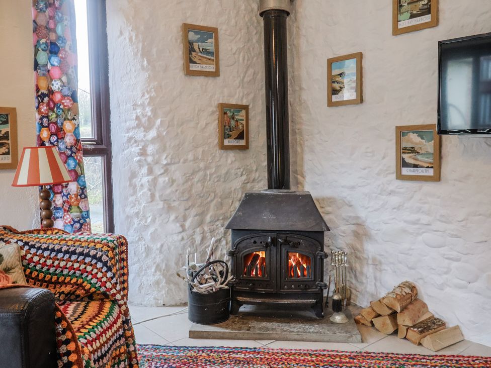 A living room with a wood stove and decorative pictures at Honeypot Cottage in Whitchurch Canonicorum
