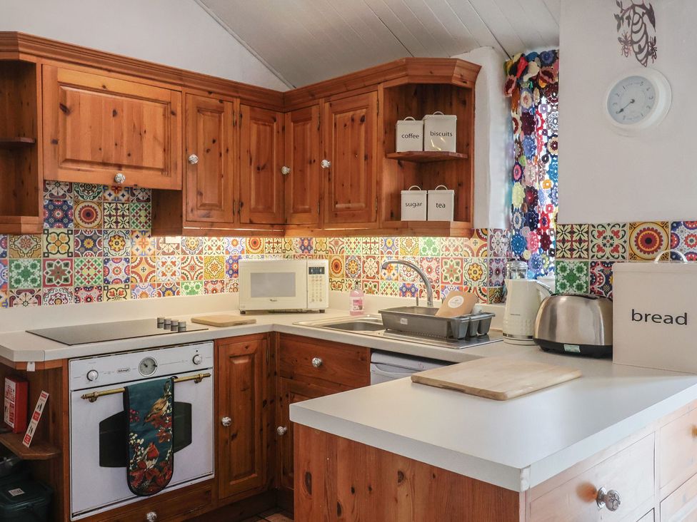 A kitchen with wooden cabinets and colorful tiles at Honeypot Cottage Whitchurch Canonicorum