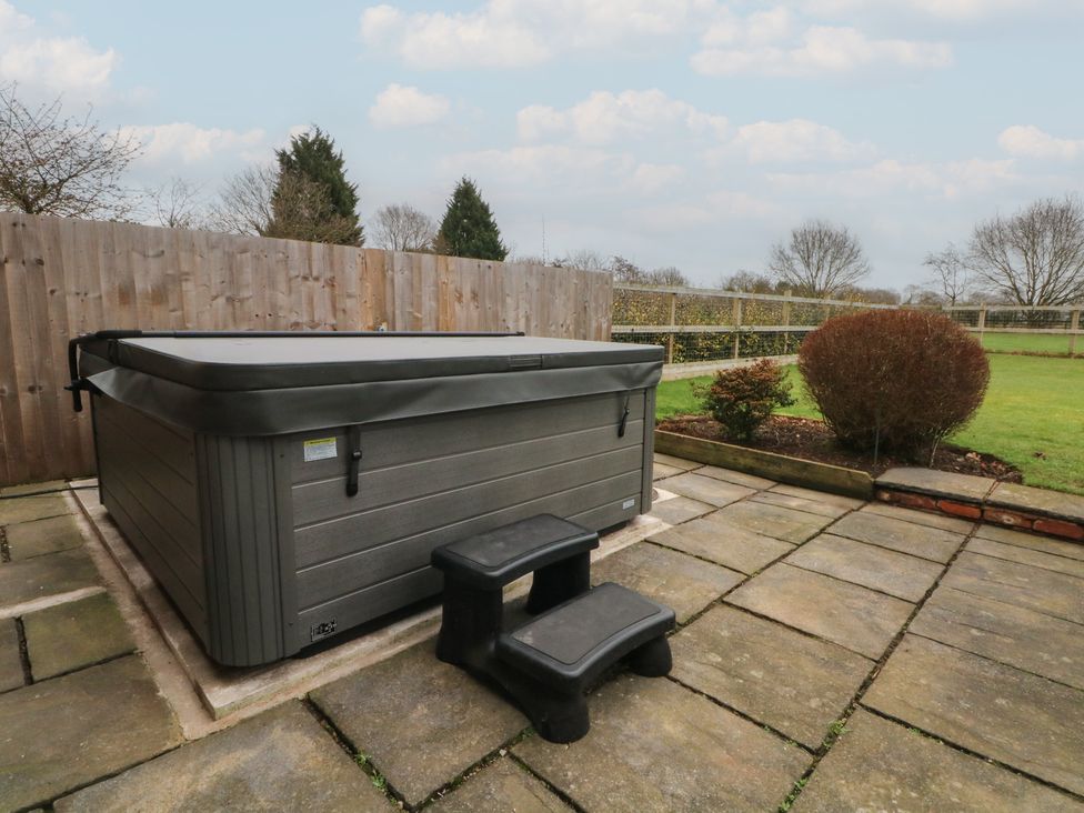 A hot tub with steps adjacent on a patio in the garden at The Winnows in Knutsford