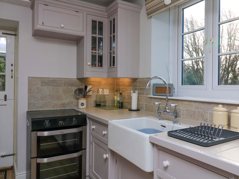 A kitchen with an oven, sink, and window at Blackstone Cottage in Salcombe