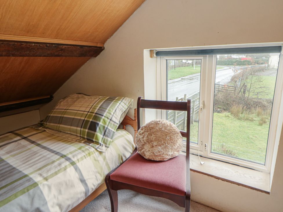 A bedroom with a bed and a chair at Glanyrafon Smithy in New Quay