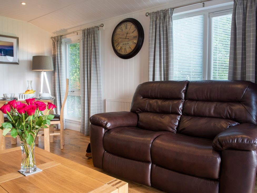 A living room with a brown sofa and flowers on a table at Nethermill Lodges in Port Glasgow