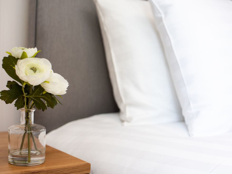 A bedside table with a vase of flowers and pillows in a bedroom at Nethermill Lodges Port Glasgow