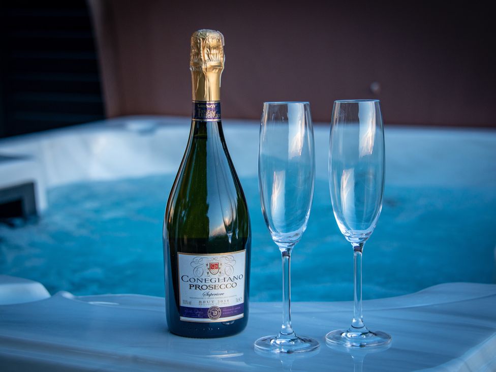 A bottle of Prosecco with two champagne glasses next to a hot tub at Nethermill Lodges in Port Glasgow