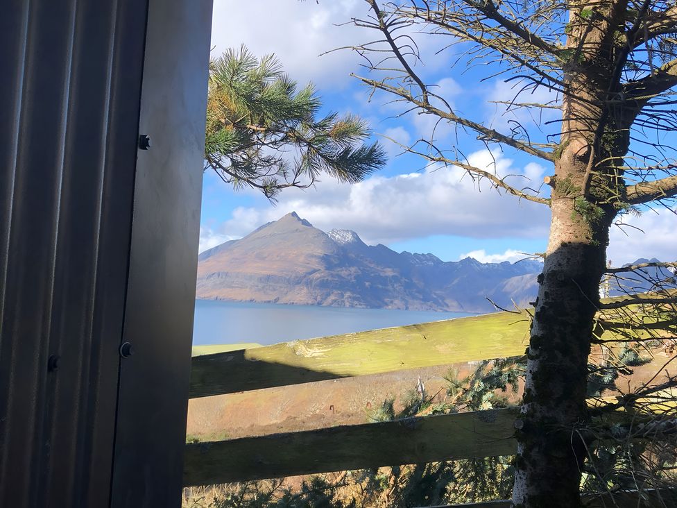 A mountain view near water with trees and a fence at Cullinview in Isle of Skye