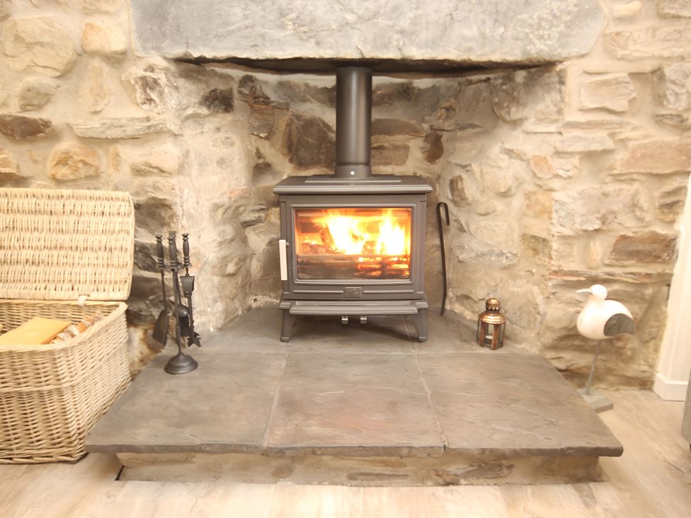 A living room with a wood stove and stone wall at Zen Cottage in Buckie