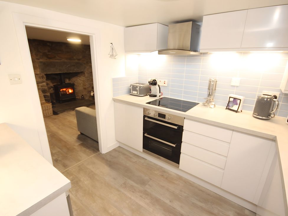 A kitchen with appliances and a view of a fireplace at Zen Cottage in Buckie