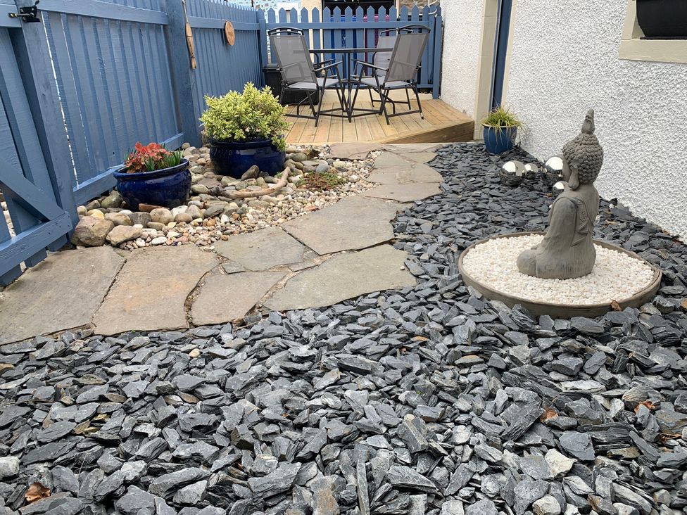 A garden with gravel, a buddha statue, and a seating area at Zen Cottage in Buckie