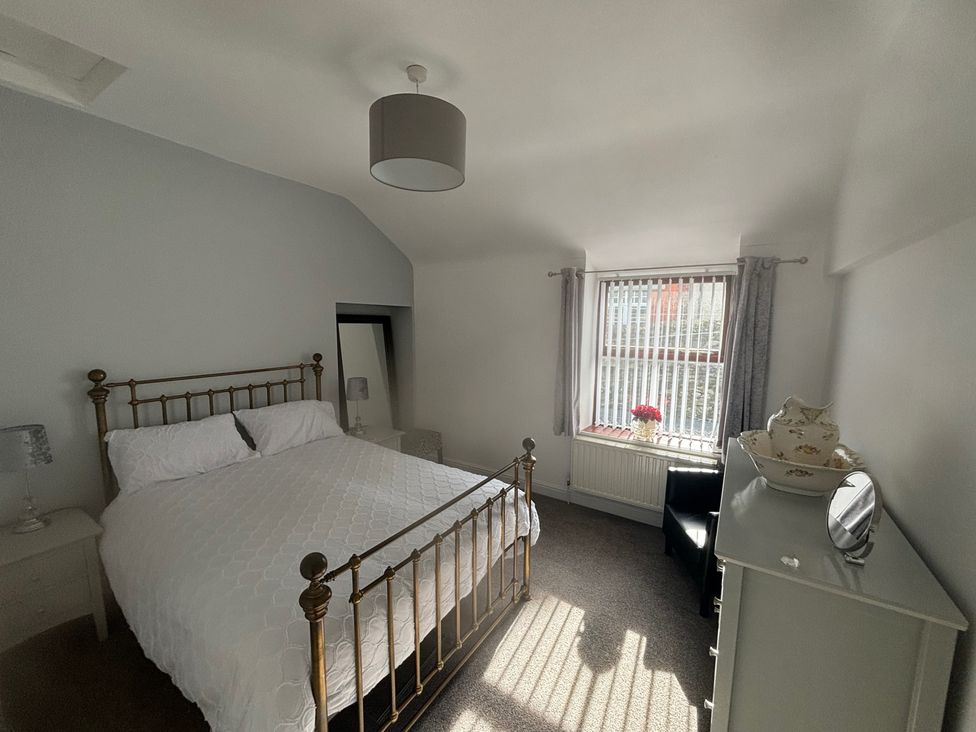 A bedroom with a bed, nightstand, chair, and window at Penmaenmawr Coastal Retreat