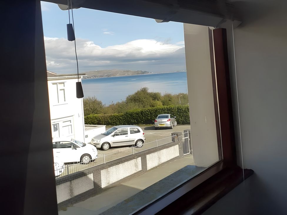 A view through a window showing a landscape with sea and cars at Penmaenmawr Coastal Retreat