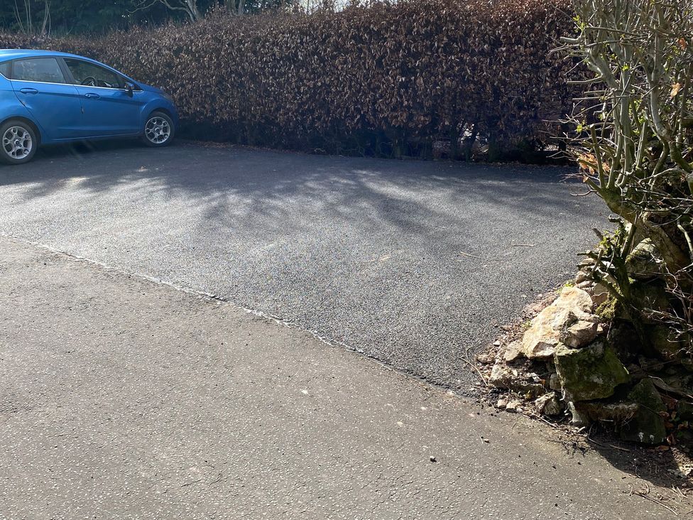 An outdoor parking area with a blue car and a hedge at The Haven in Penrith
