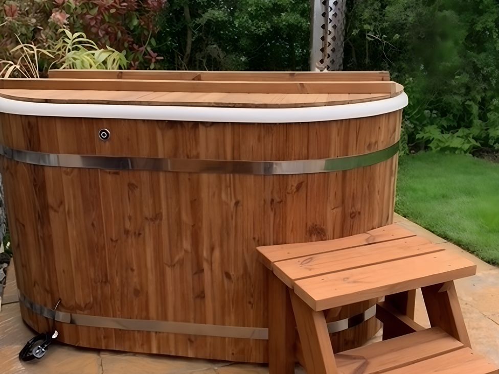 A hot tub with a wooden bench in a garden at Cosy Escape in Sheerness