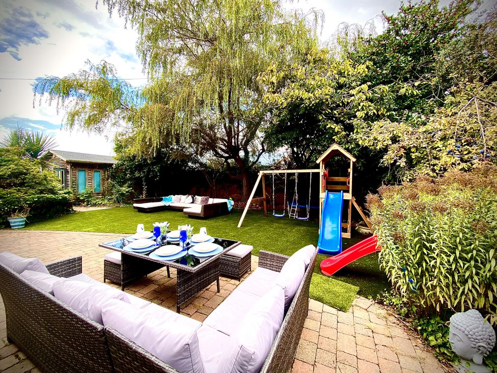A garden with a sofa, swing set, slide, and table at Anchor Hot Tub Suite in Lytham St. Annes