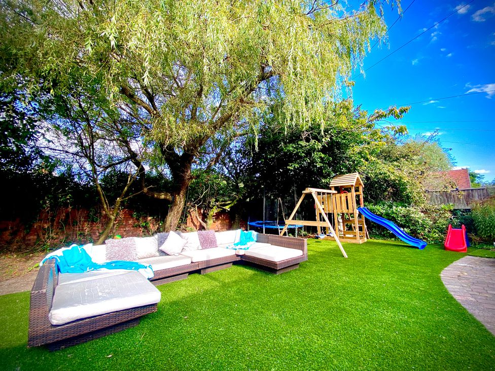 A garden with a sofa, swing set, slide, and trampoline at Anchor Hot Tub Suite in Lytham St. Annes