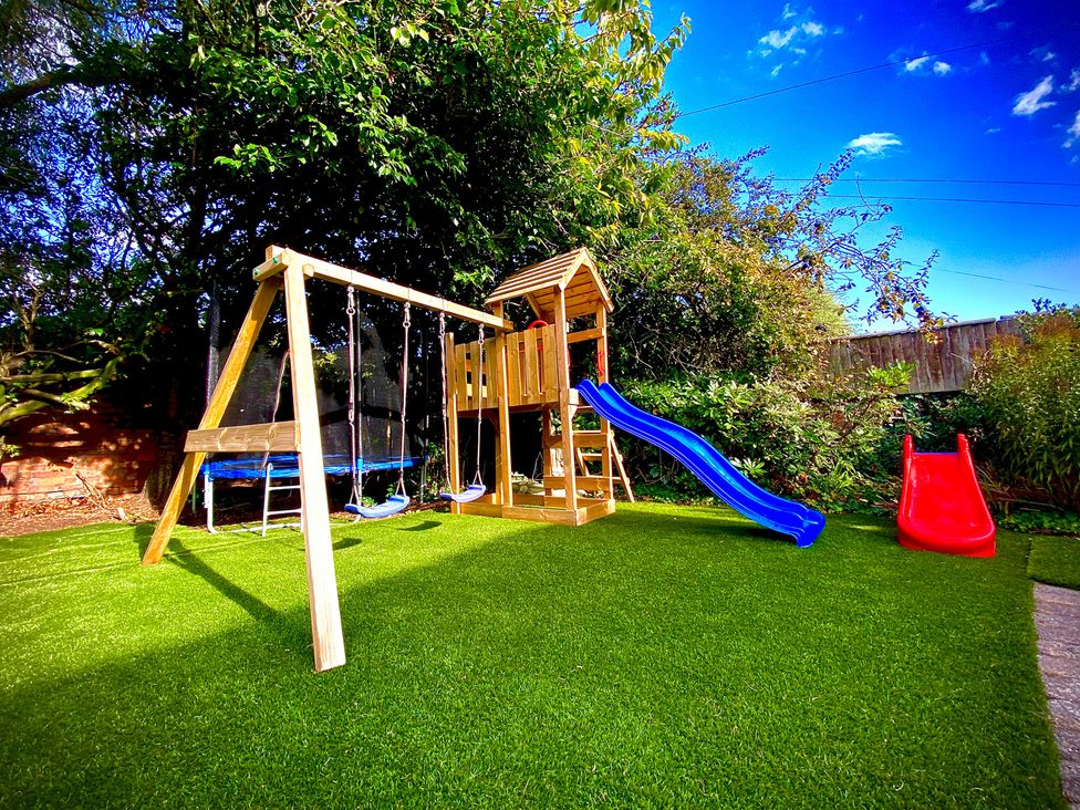 A garden with a playhouse, swings, blue slide and red slide at Anchor Hot Tub Suite Lytham St. Annes