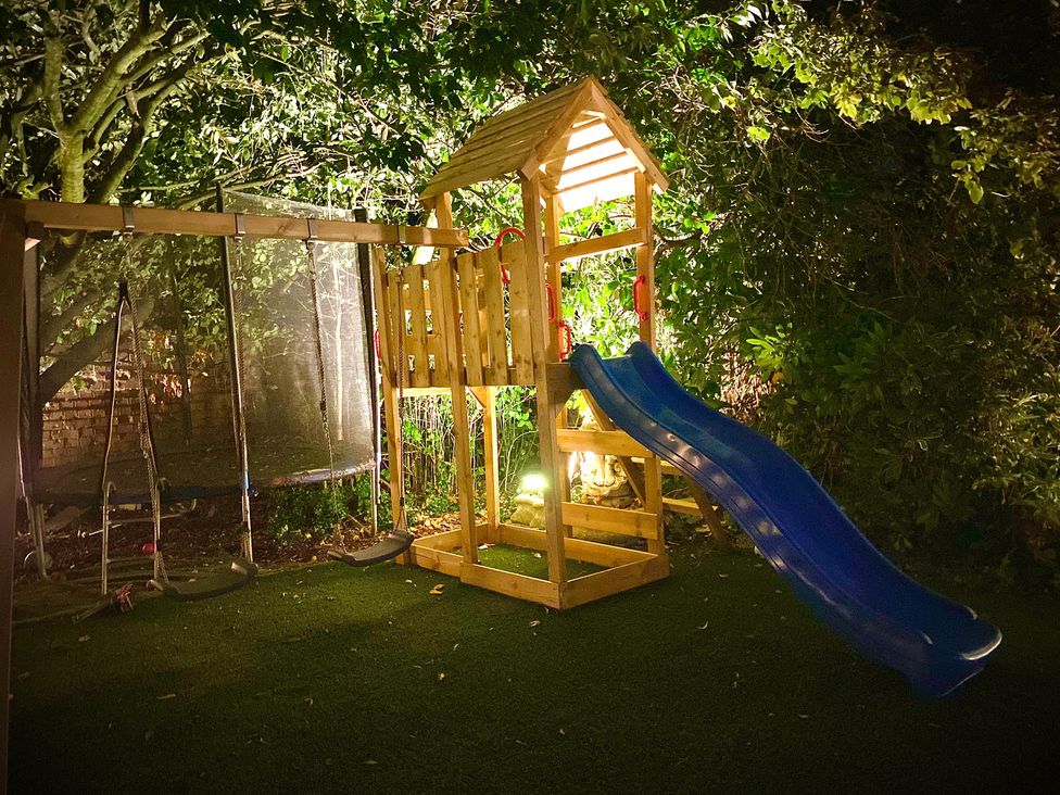 A play structure with a slide and swings in a garden at Anchor Hot Tub Suite in Lytham St. Annes