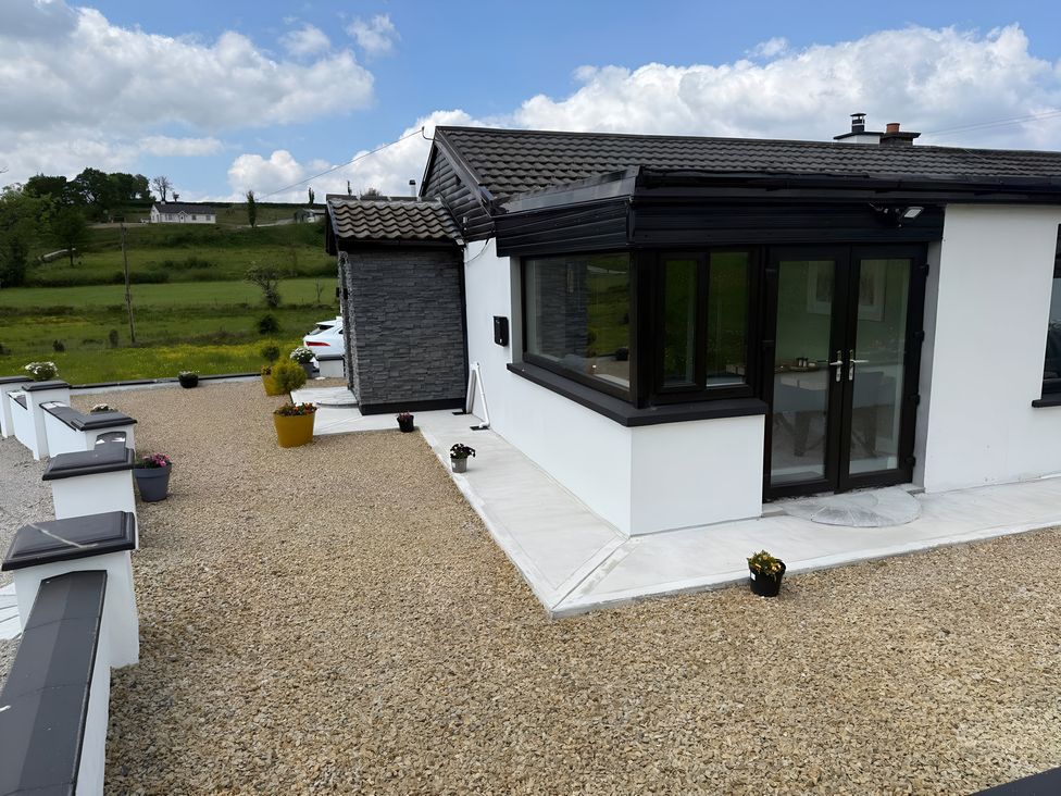 An outdoor area with a house, gravel driveway, and planters at Cherry Chirp Cottage in Enniskillen
