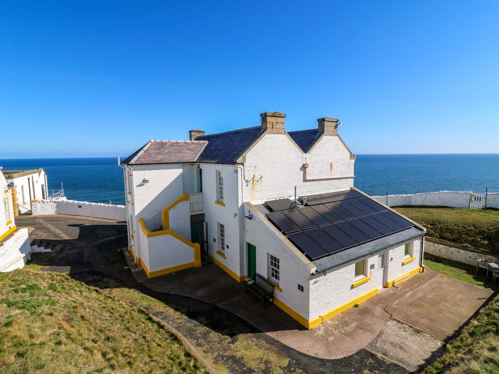 A building with solar panels and a bench overlooking the ocean at The Lighthouse Retreat in St Abbs