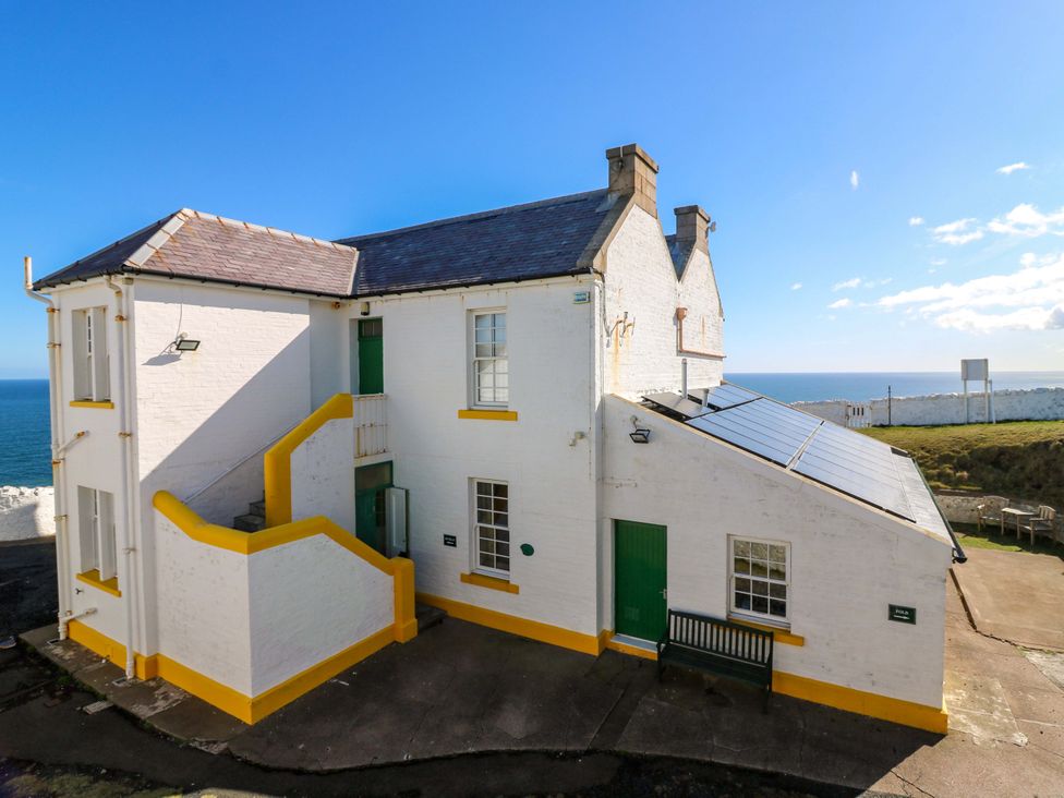 A white building with a green door and solar panels at The Lighthouse Retreat in St Abbs