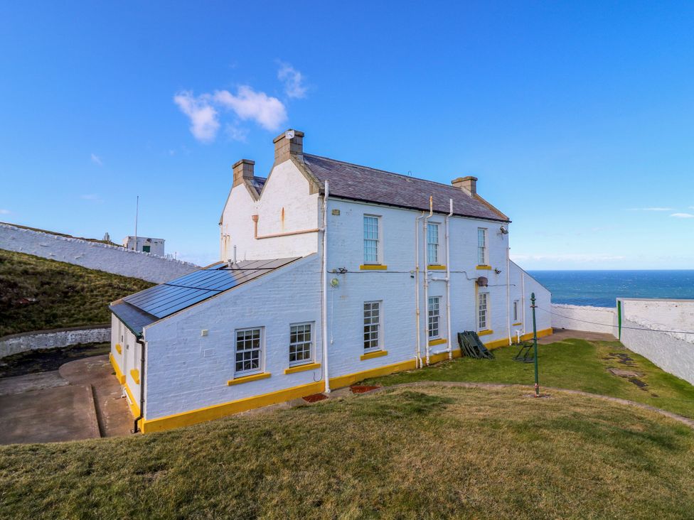 An exterior view of a white building with a lawn and ocean at The Lighthouse Retreat in St Abbs