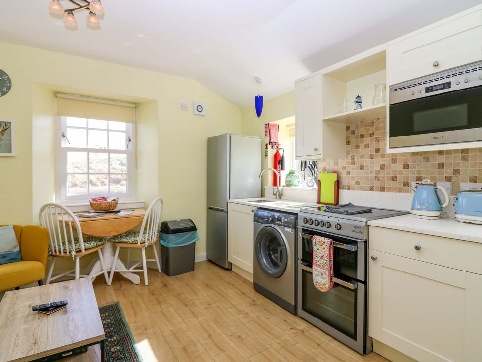 A kitchen with refrigerator, washing machine, and table at Keepers Fold at The Lighhouse in St Abbs
