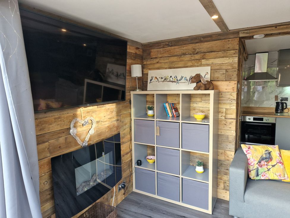 A living room with a television, bookshelf, and sofa at Birdsong lodge near Hawthorn Farm near Sutton-On-Sea