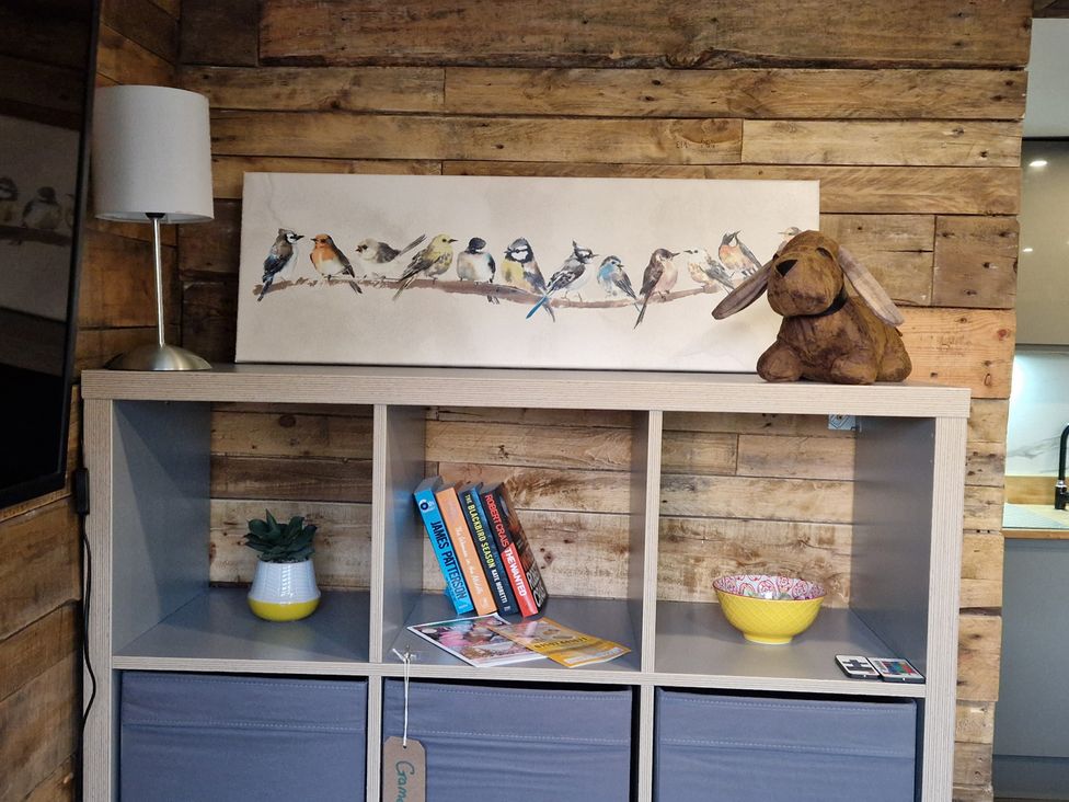 A living room with a shelf holding books and a lamp at Birdsong lodge near Hawthorn Farm near Sutton-On-Sea