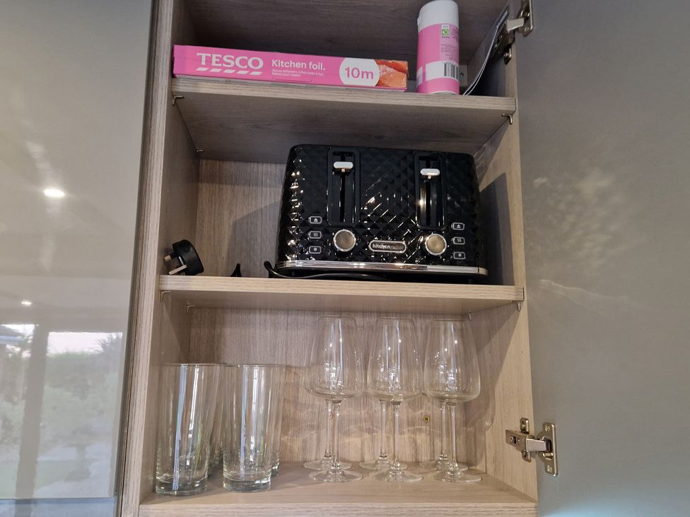 A kitchen cabinet with a toaster and various types of glasses at Birdsong lodge near Sutton-On-Sea