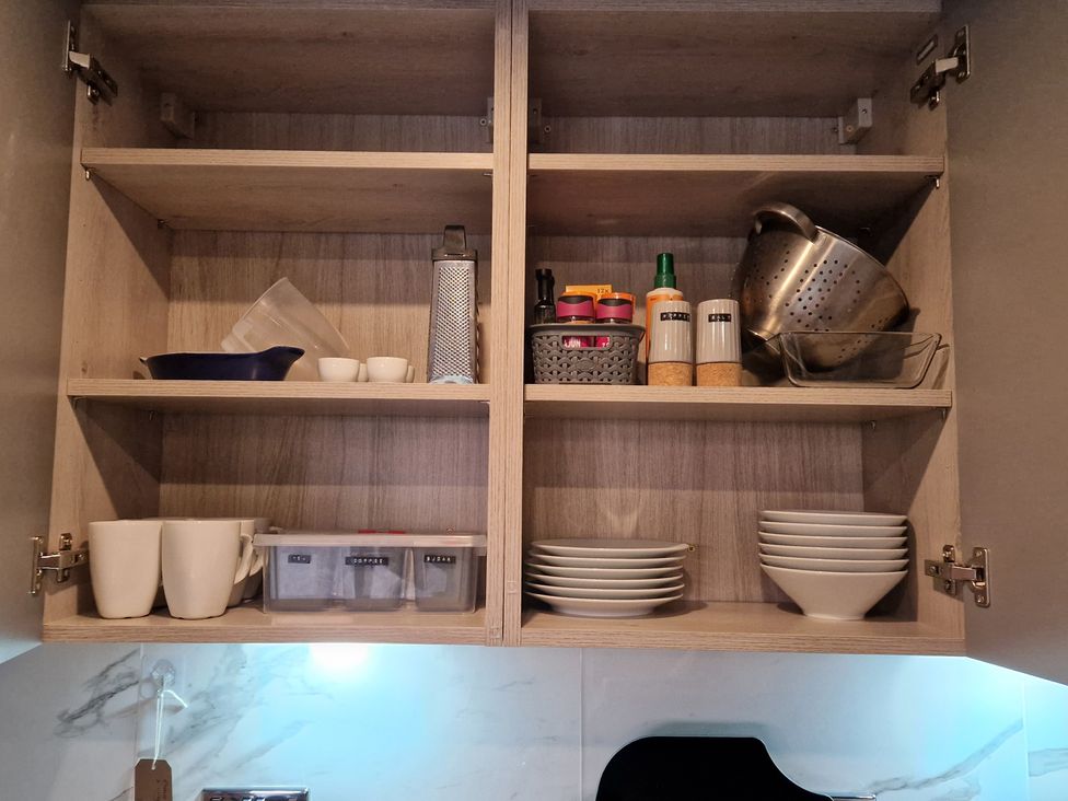 A kitchen cabinet with cups, plates, and storage containers at Birdsong lodge near Hawthorn Farm near Sutton-On-Sea
