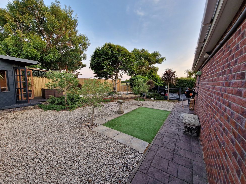 A garden with gravel, artificial grass, and trees at Birdsong lodge near Hawthorn Farm near Sutton-On-Sea