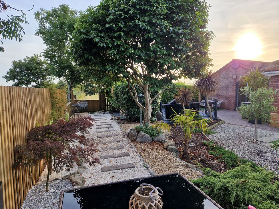 A garden with a pathway and trees at Birdsong lodge near Hawthorn Farm near Sutton-On-Sea