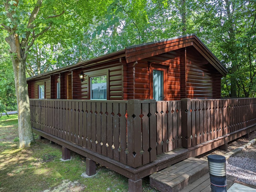A wooden cabin with a porch surrounded by trees at Pineshadow Lodge in Louth