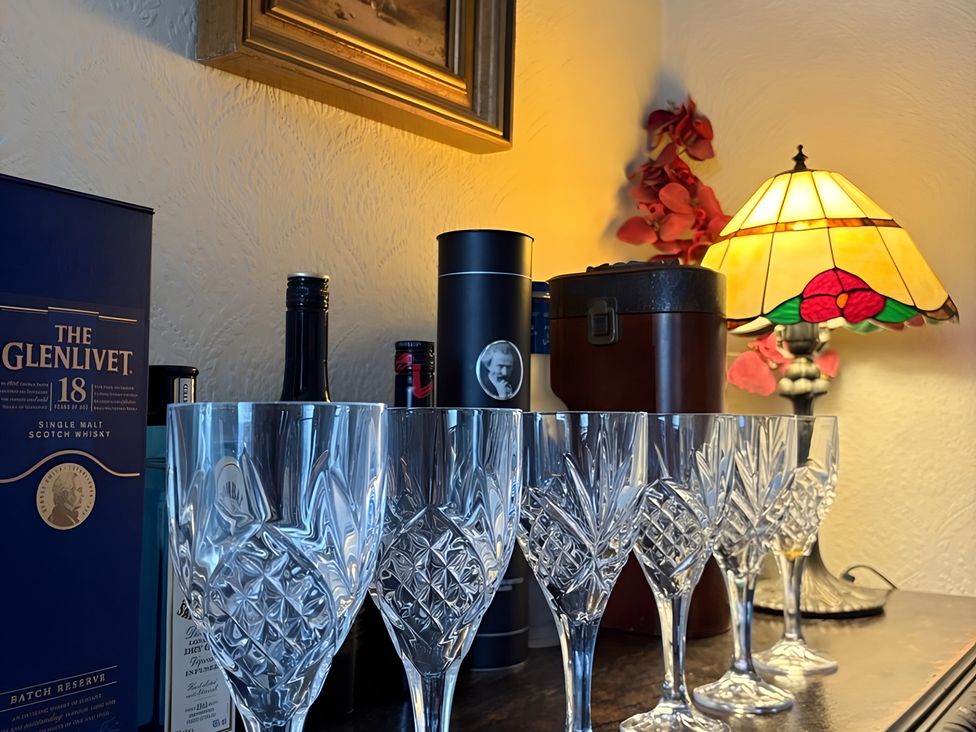 A display of whiskey bottles and crystal glasses with a lamp at Fountain Hill House in Londonderry