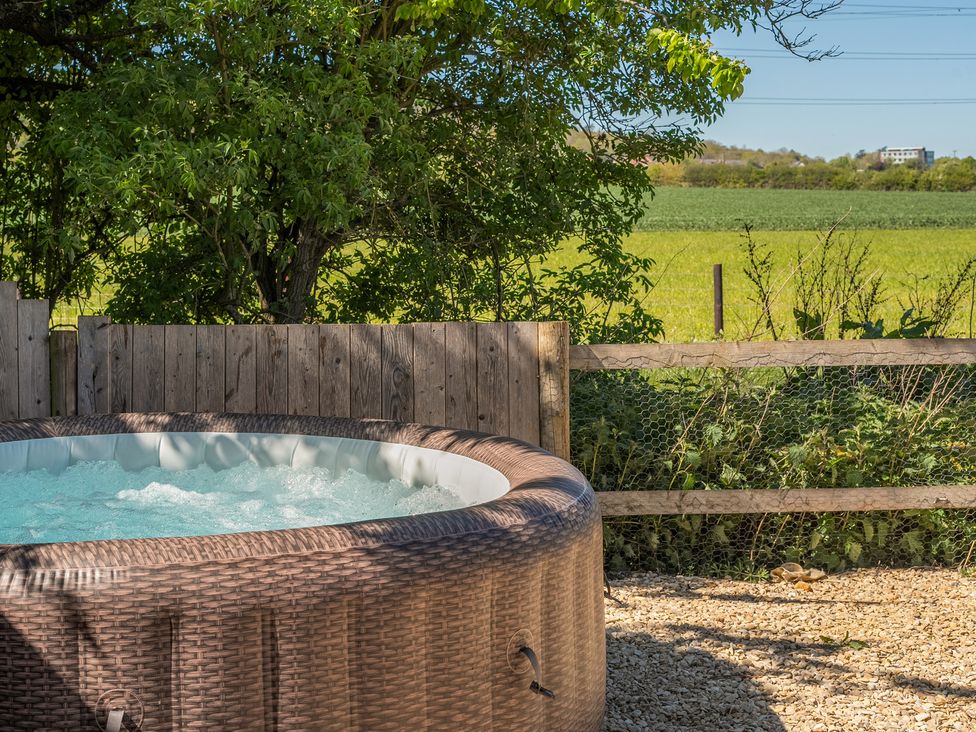 A hot tub with a wooden fence and greenery at Cotswold Nights in Ashton Under Hill