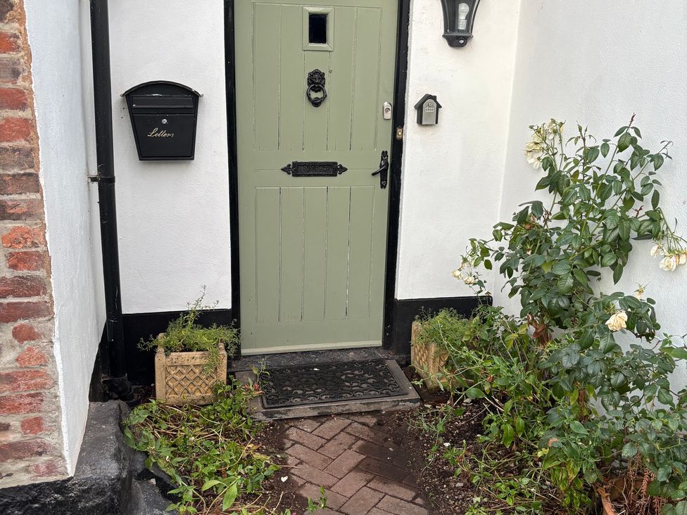 An entrance with a green front door and plants at The Olde Forge in Carhampton near Minehead